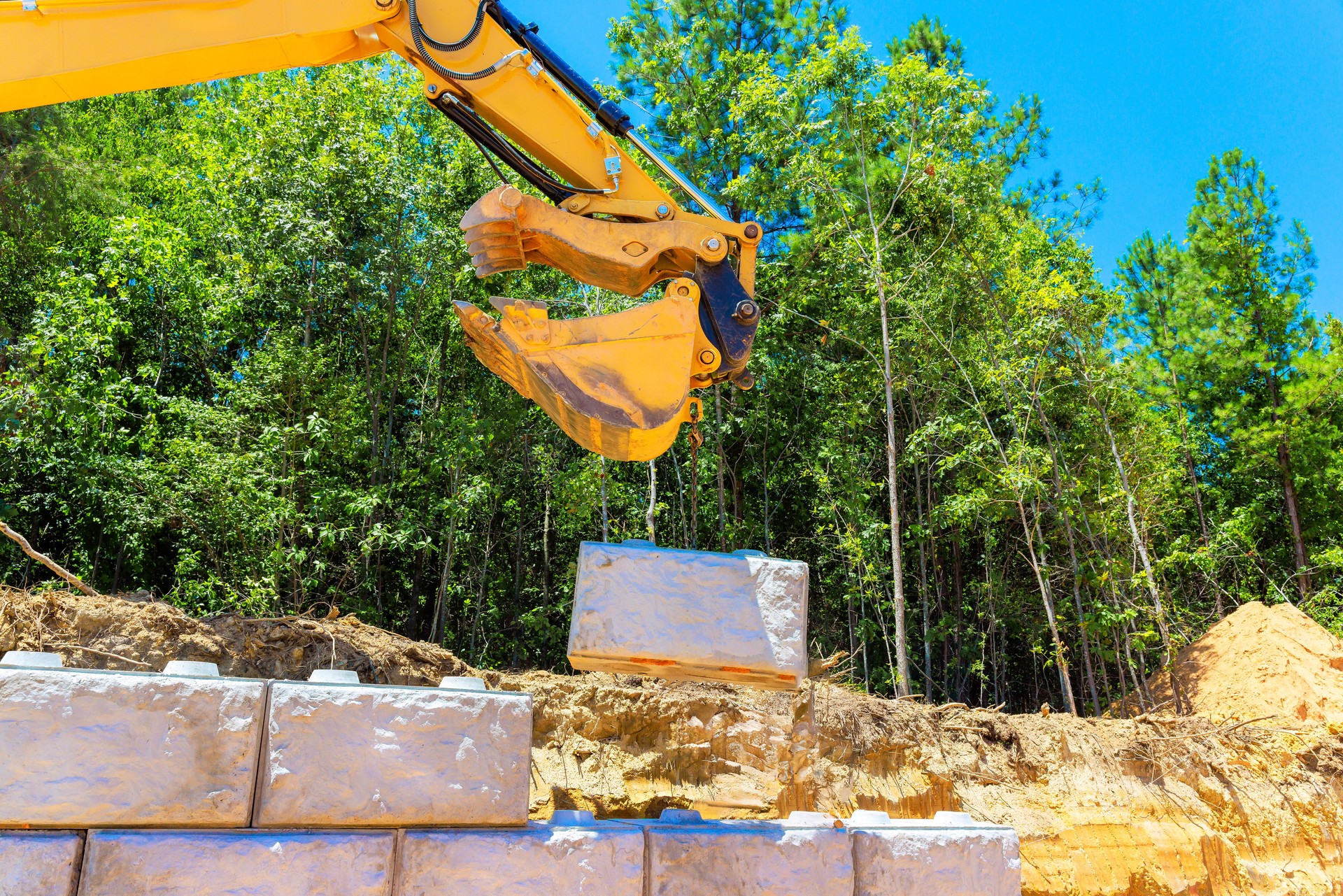 Heavy machinery lifts stone block at construction site surrounded by lush trees on works day